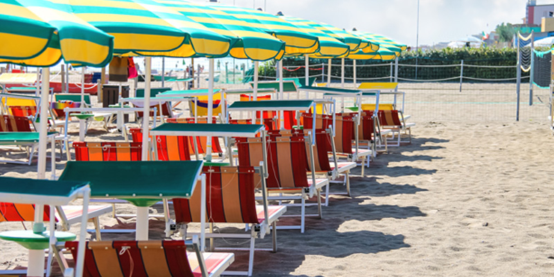 Le sdraio rosse e giallo sono disposte con ordine sulla spiaggia di sabbia fine di Bellaria. Sullo sfondo si intravede un campo di beach volley.