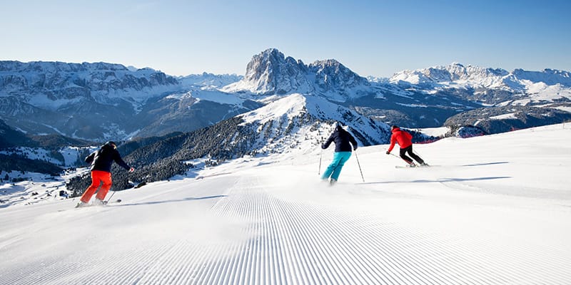 due persone sciano sulle piste bianche della Val Gardena, circondati dalle montagne innevate.