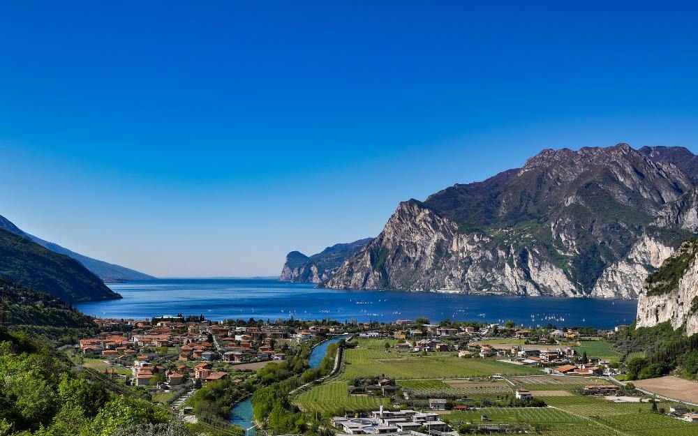 Il lago incontra la verde vallata delimitata dalle montagne. Sulle sponde del lago sorge la cittadina di Riva del Garda.