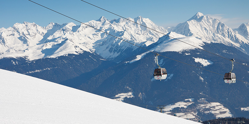 La cabinovia di Plan de Corones avanza con le Alpi innevate sullo sfondo. In primo piano si intravede la superficie innevata nella montagna.